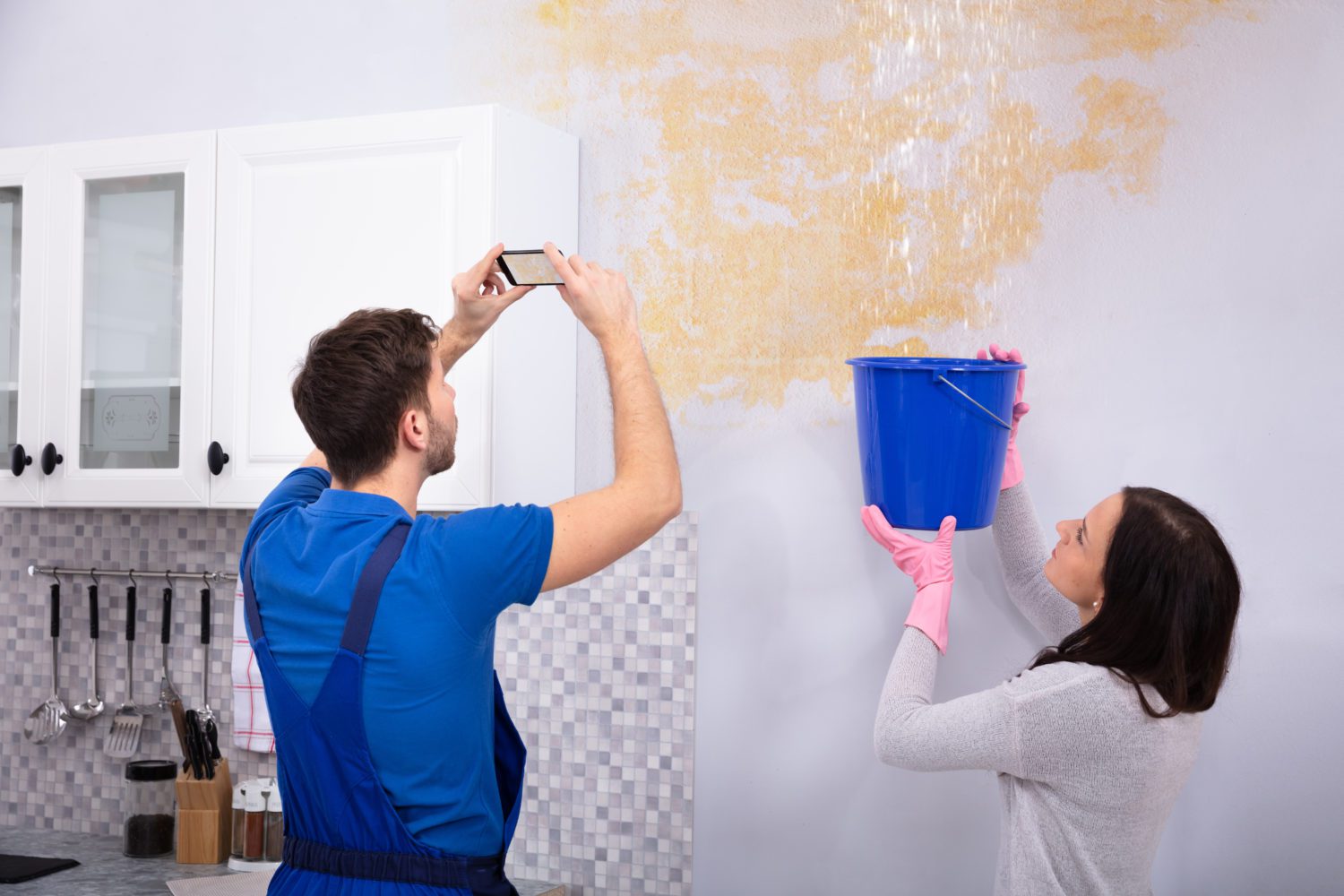 Woman,Collecting,Water,In,Blue,Bucket,From,Damaged,Ceiling,While